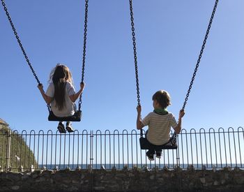 Rear view of children sitting on swing at playground