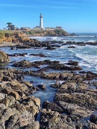 Lighthouse on beach by sea against sky