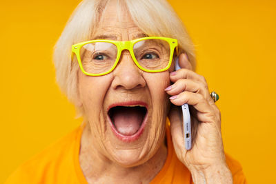 Smiling senior woman talking on phone against yellow background