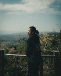 Side view of young woman looking away against sky