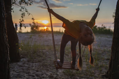 Happy girl having fun at swing at sunset by the sea in autumn, family walking in nature, fall vibes