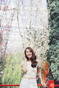 Portrait of smiling young woman standing against plants