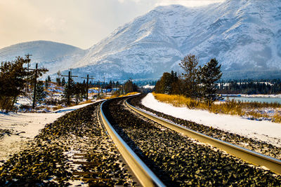 Railroad tracks by snowcapped mountain against sky