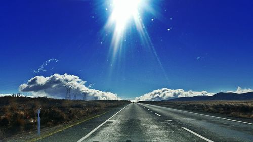 Country road leading towards mountains against blue sky