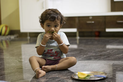 Boy sitting on a marble stone eating mangoe and keeping chopped mangoes in a palette near the child.