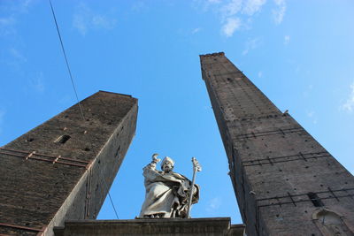 Low angle view of statue amidst towers against blue sky