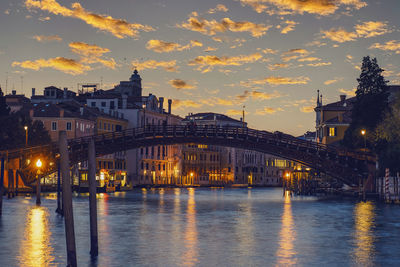 Illuminated bridge over river against sky at sunset