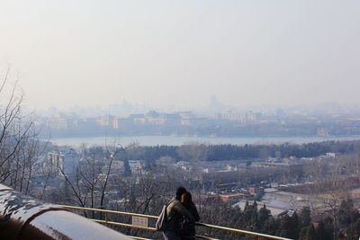 People standing on bridge in city against sky during winter