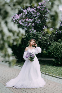 Beautiful bride in a wedding dress walks in a blooming apple-tree park in spring