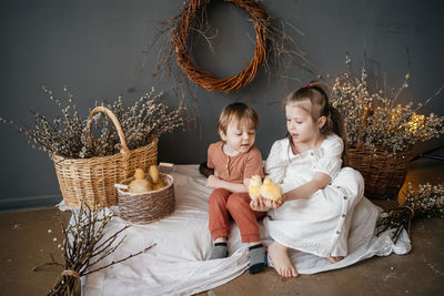 Brother and sister with small goslings in a wicker basket eco style gray willow background