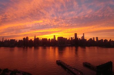 Silhouette buildings by river against sky during sunset over manhattan - new york city