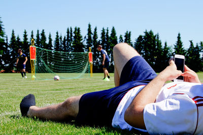 Close-up of man using mobile phone while lying on soccer field