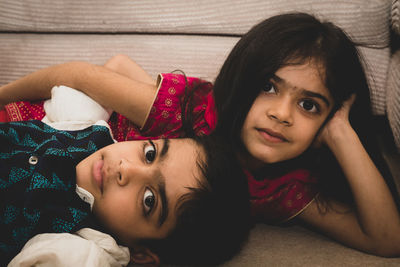 Portrait of cute siblings lying on sofa at home