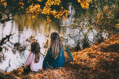 Rear view of women and daughter sitting by a pond during autumn