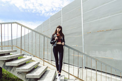 Thoughtful young woman standing on steps against wall