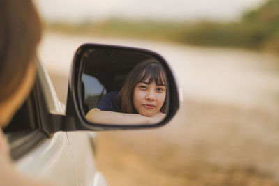 Portrait of woman with reflection on side-view mirror
