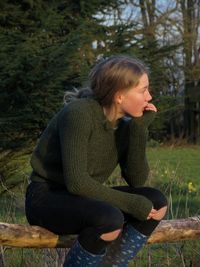 Thoughtful teenage girl sitting on log against trees in forest