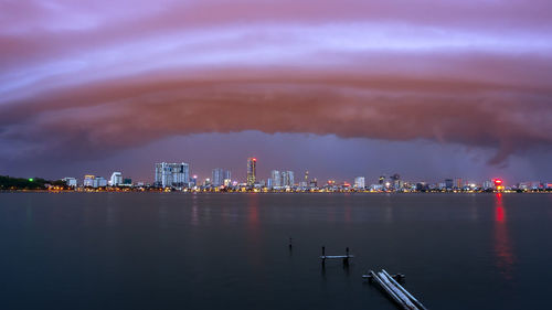 Sea by illuminated city against sky at night