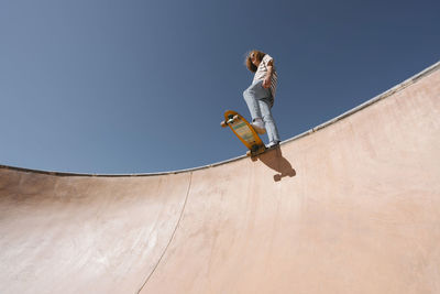 Young man with skateboard at sports ramp on sunny day