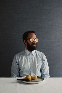 Man wearing eyeglasses sitting at table against gray wall
