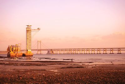 Suspension bridge over sea against sky during sunset