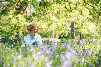 Thoughtful woman sitting amidst plants in forest on sunny day