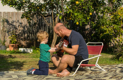 Full length of man teaching guitar to son in backyard
