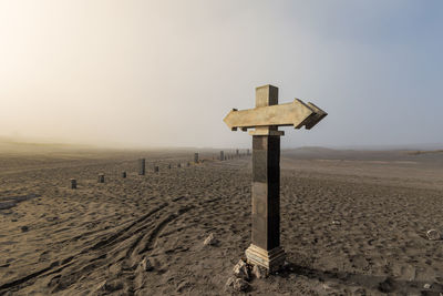 Stone sign post with opposite arrows and copy space in dry landscape and dirt road, java, indonesia