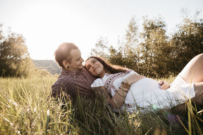 Couple relaxing on grassy field against clear sky at park