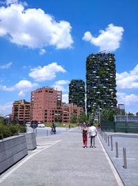 People walking by buildings in city against sky