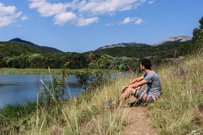 A young man is walking alone by the lake with a mountain landscape