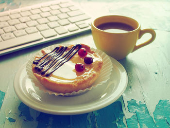 High angle view of coffee cup and tart with computer keyboard on wooden table
