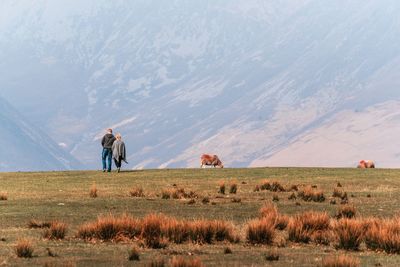 Rear view of couple walking on field against mountain