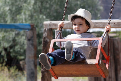 Full length of cute boy sitting on swing at playground