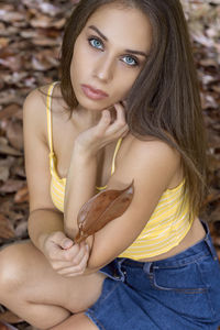 Portrait of beautiful young woman holding dry leaf while crouching
