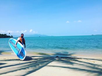 Man with surfboard standing at beach against sky