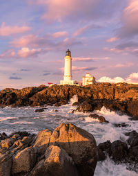 Lighthouse by sea and buildings against sky