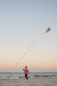 Boy at beach with kite flying against sky during sunset