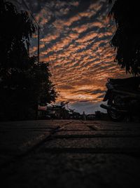 Road by trees against sky during sunset