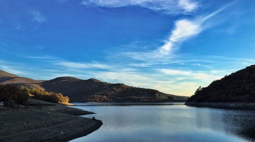 Scenic view of river by mountains against blue sky