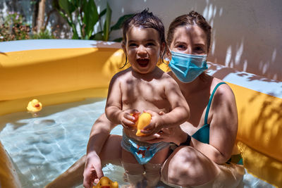 Young mother with a mask in an inflatable pool with her little daughter. safe holiday concept