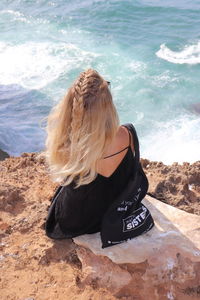 Rear view of woman sitting on rock at beach