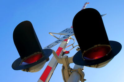 Low angle view of railroad crossing sign against clear blue sky