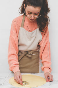 Beautiful caucasian teenage girl cuts out shortbread dough with a metal heart shape .