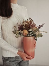 Midsection of woman holding flower bouquet against wall