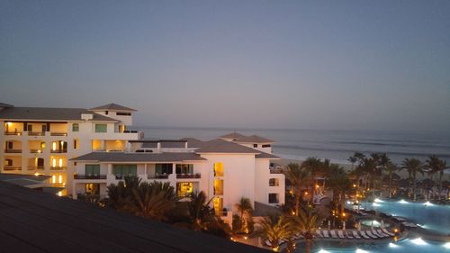 Illuminated houses by sea against sky at dusk