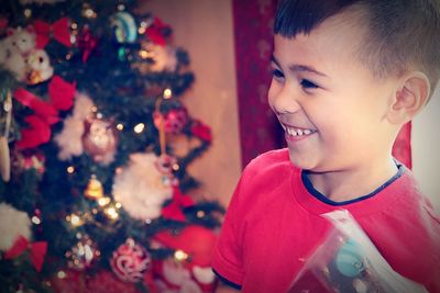 Cute cheerful boy looking away against christmas tree at home