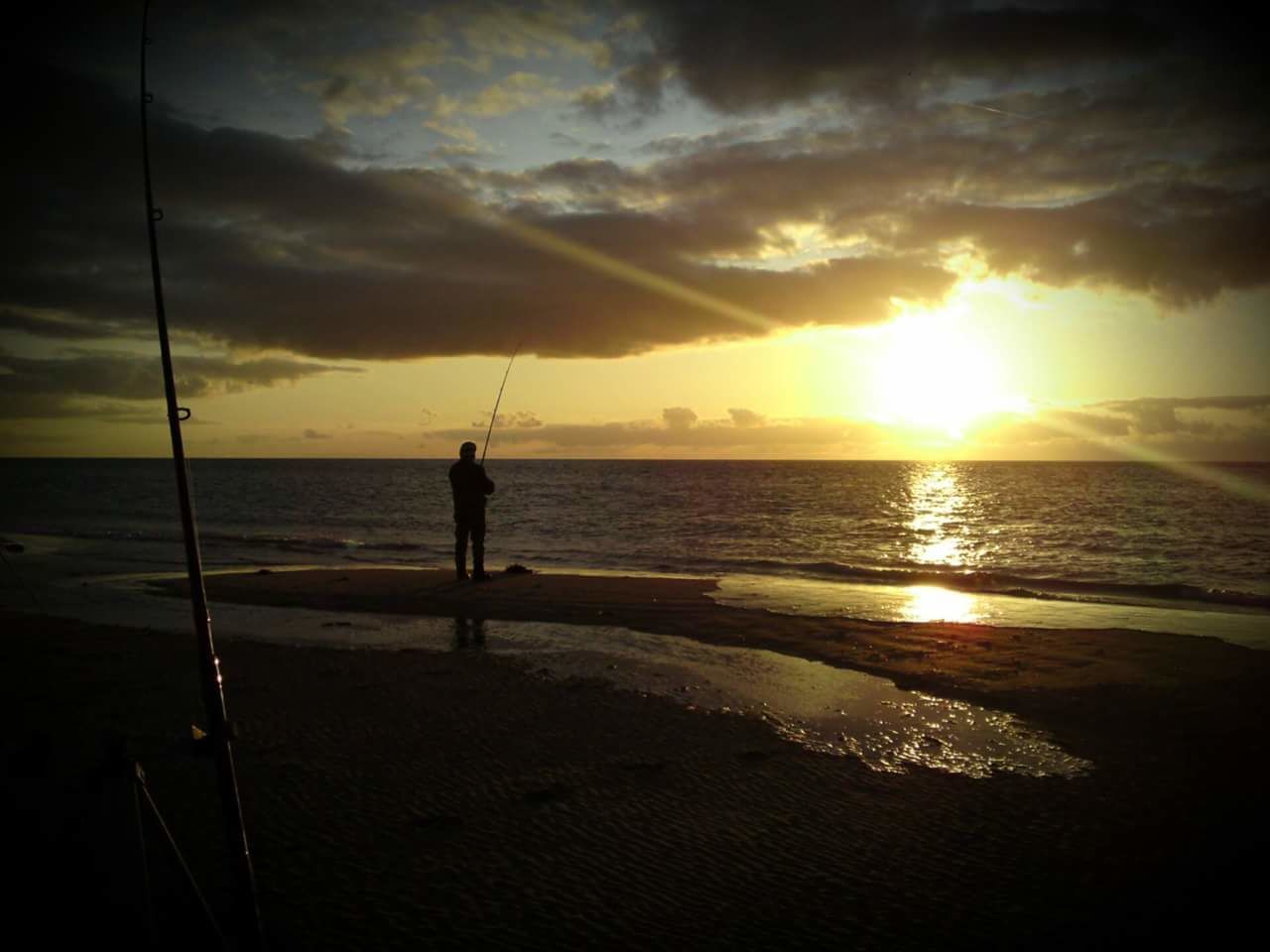 MAN FISHING AT BEACH AGAINST SKY DURING SUNSET