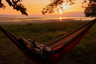 A european woman in a hammock plays the guitar at sunset and looks at nature