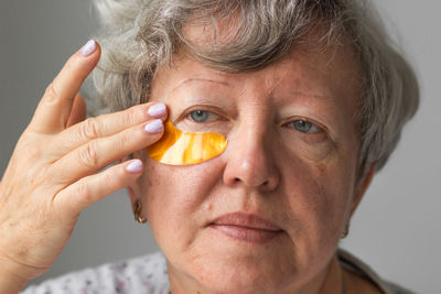 Senior woman applying hydrogel eye patches against wrinkles. gray-haired lady using cosmetics.